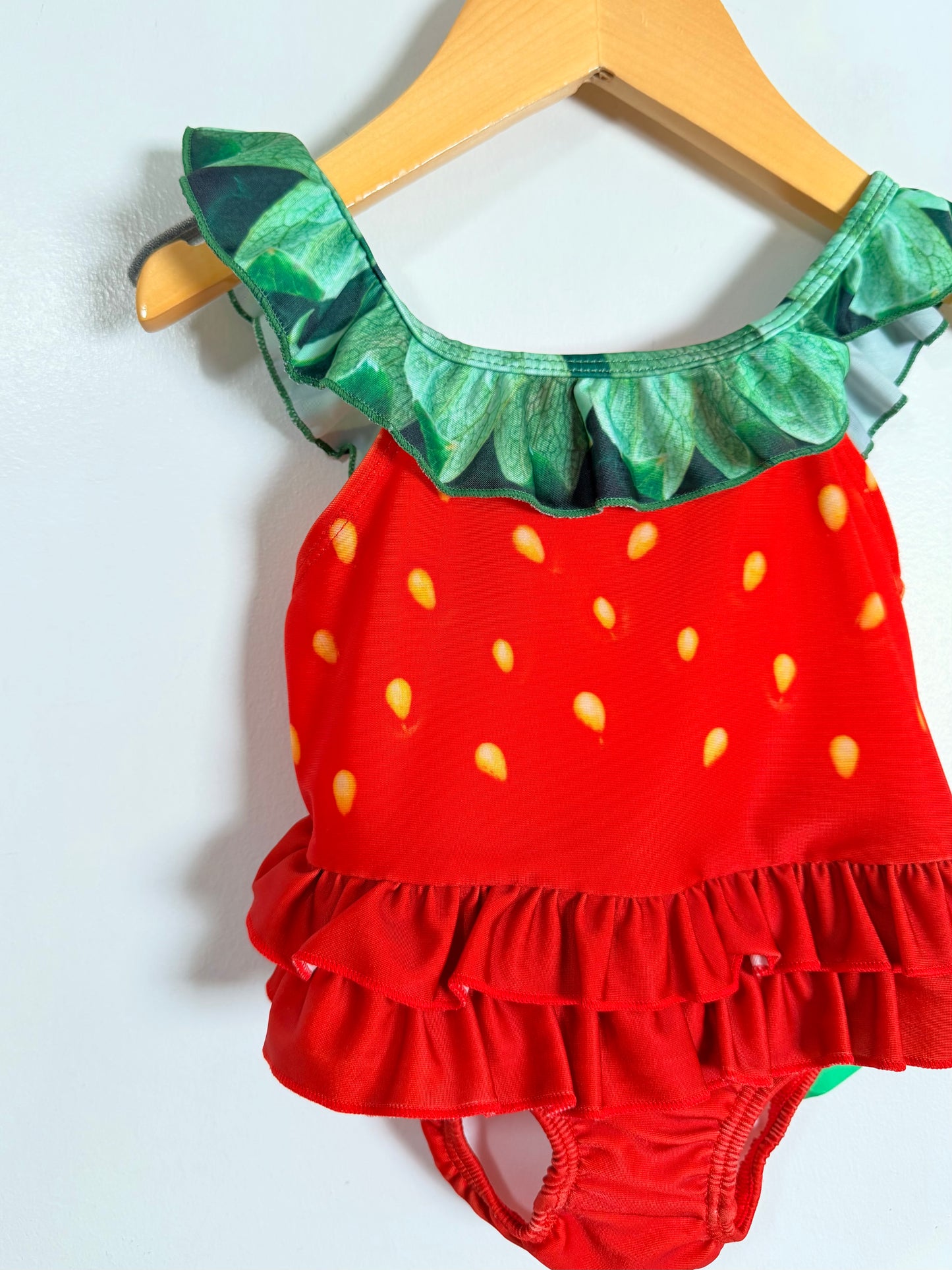 Strawberry-themed children's swimsuit with ruffled details on a hanger.