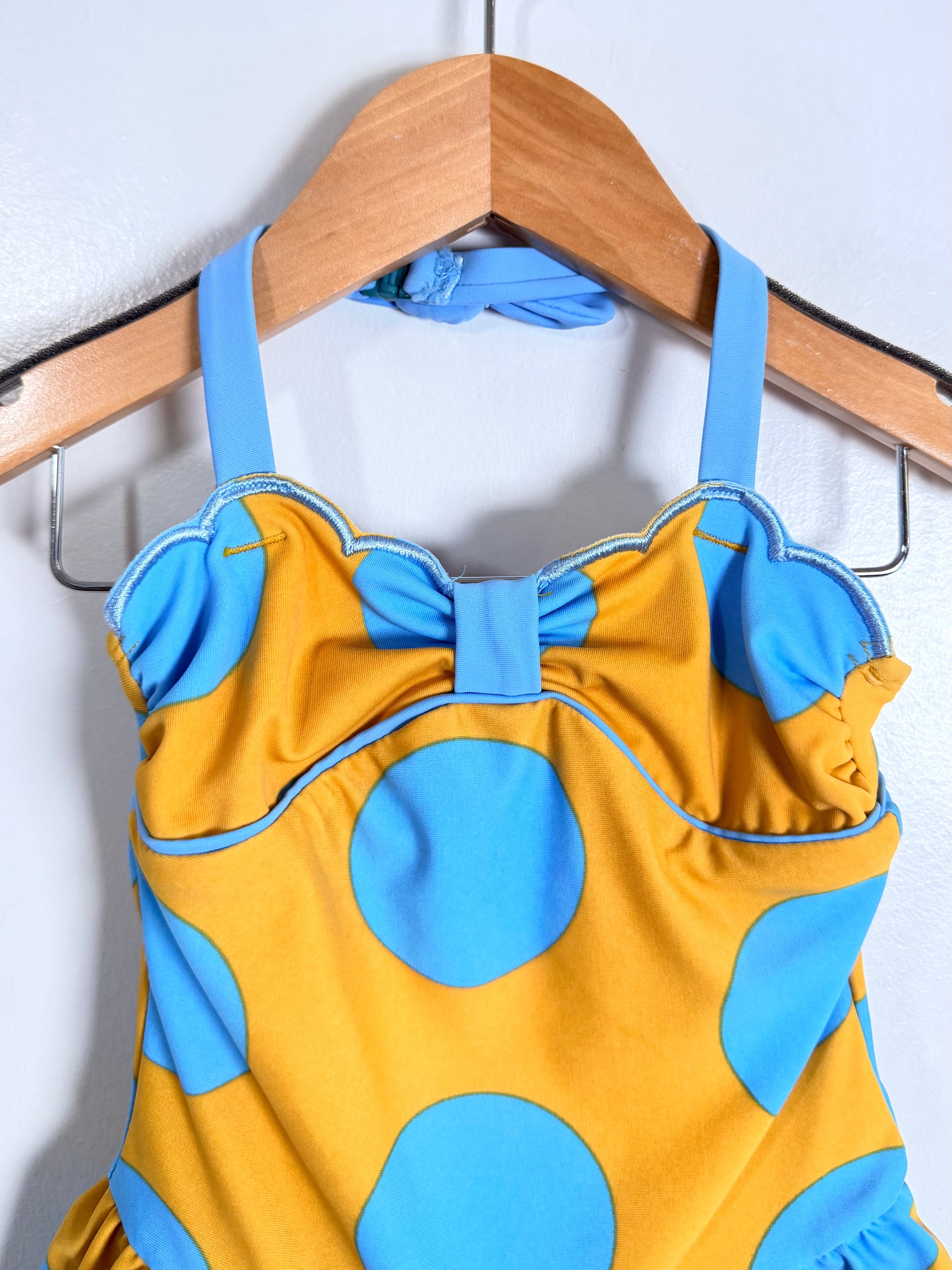 Yellow swimsuit with blue polka dots on a wooden hanger against a white background