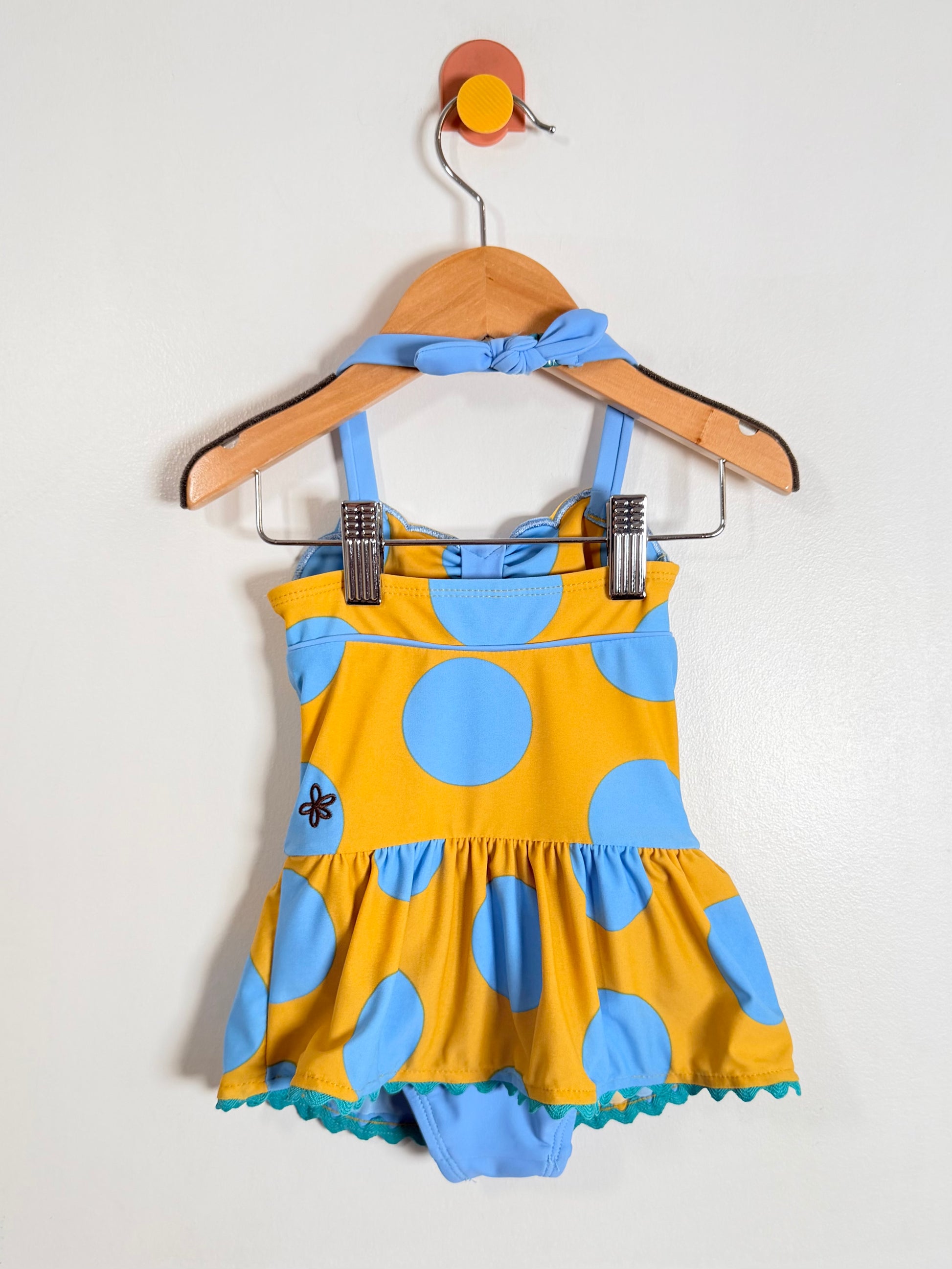 Yellow and blue polka dot dress on a hanger against a white background