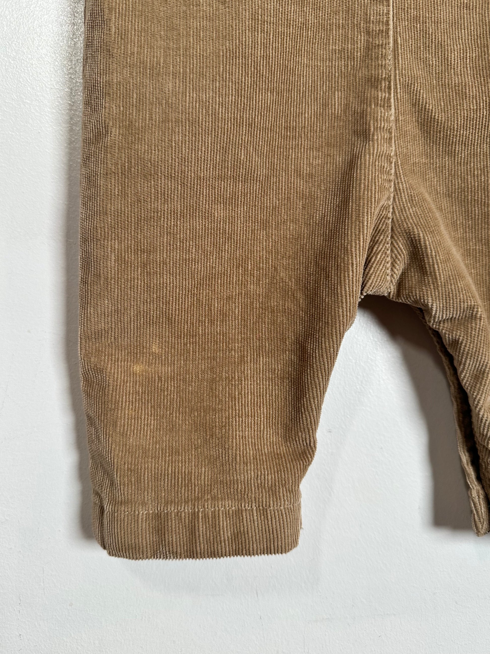 Close-up of a pair of brown corduroy pants showing the ribbed fabric texture and hem against a plain white background.