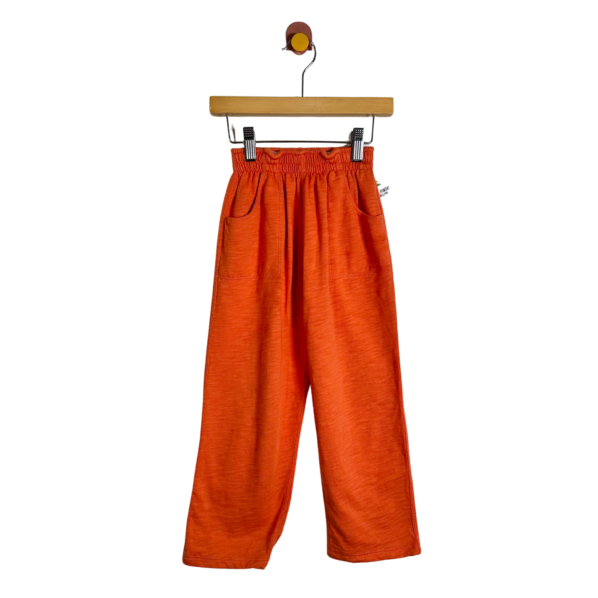 Bright orange wide-leg cropped pants with an elastic waistband and side pockets, hanging from a wooden hanger against a plain white background.