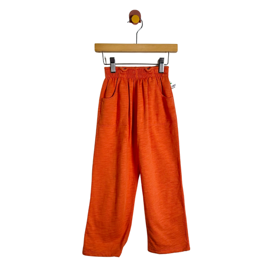 Bright orange wide-leg cropped pants with an elastic waistband and side pockets, hanging from a wooden hanger against a plain white background.