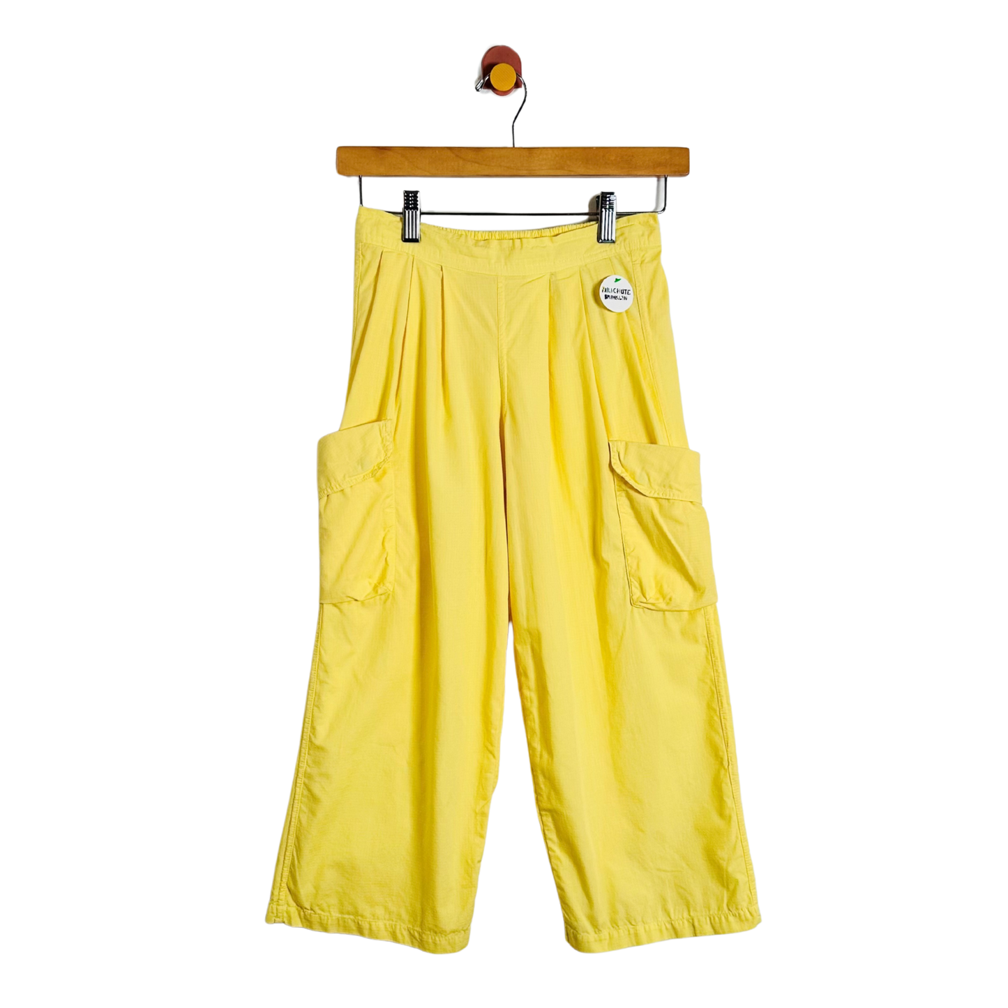 Bright yellow wide-leg cargo pants with side flap pockets, hanging from a wooden hanger against a plain white background.