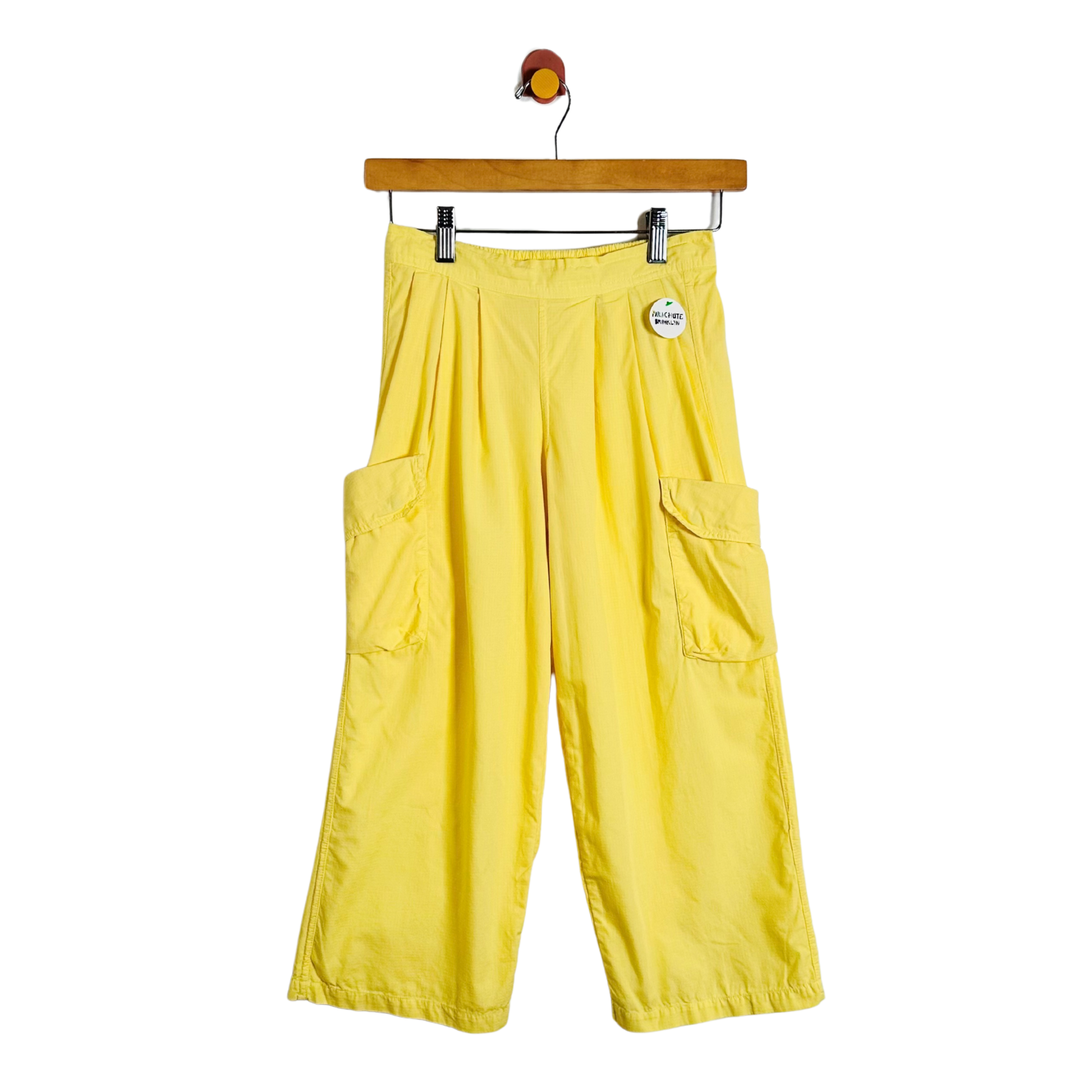Bright yellow wide-leg cargo pants with side flap pockets, hanging from a wooden hanger against a plain white background.