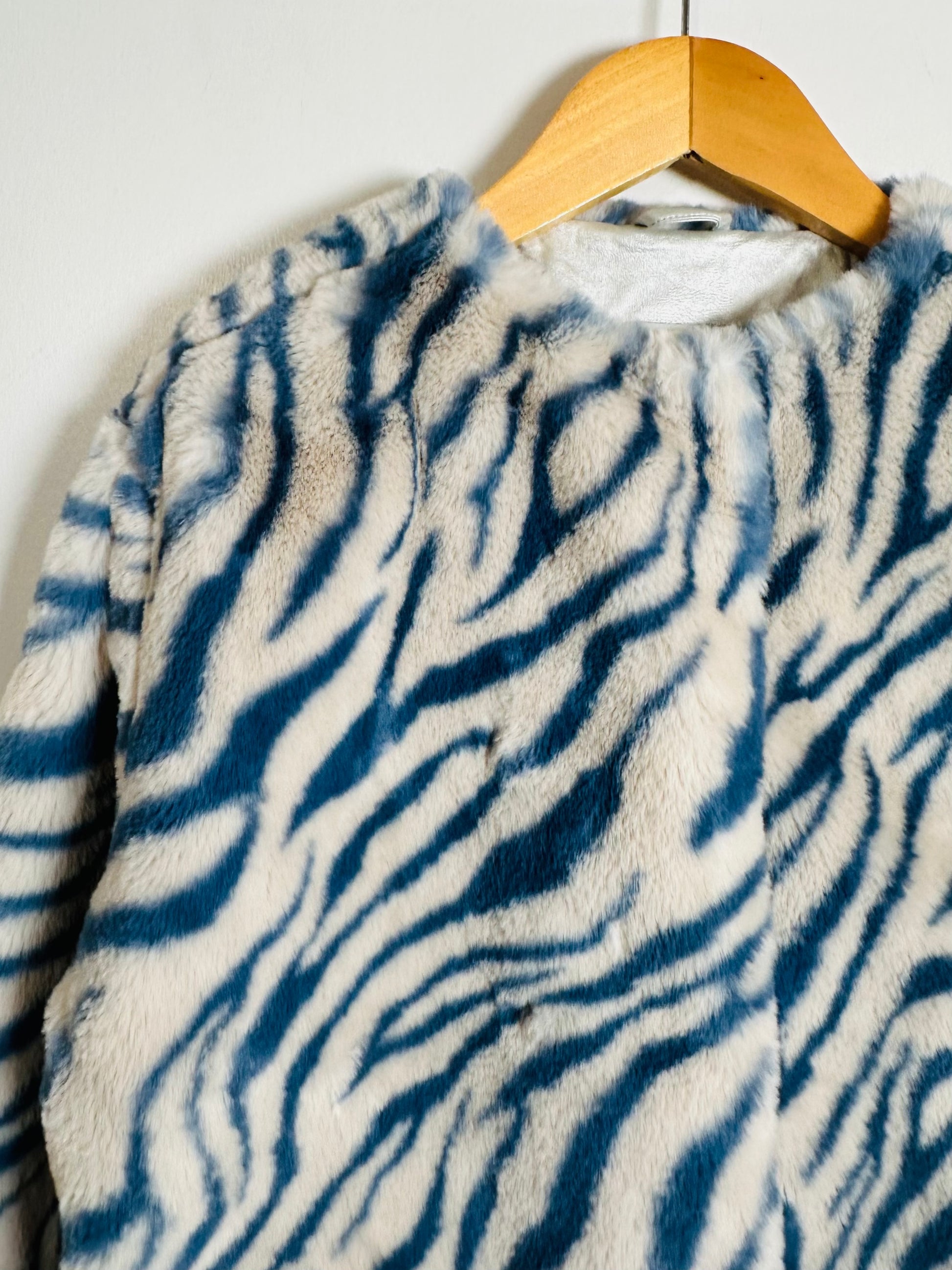 Blue and white zebra-striped coat on a wooden hanger against a white wall.