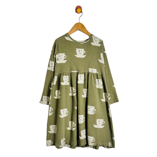 An olive green long-sleeve dress with a white coffee cup pattern, hanging on a wooden hanger against a plain white background.