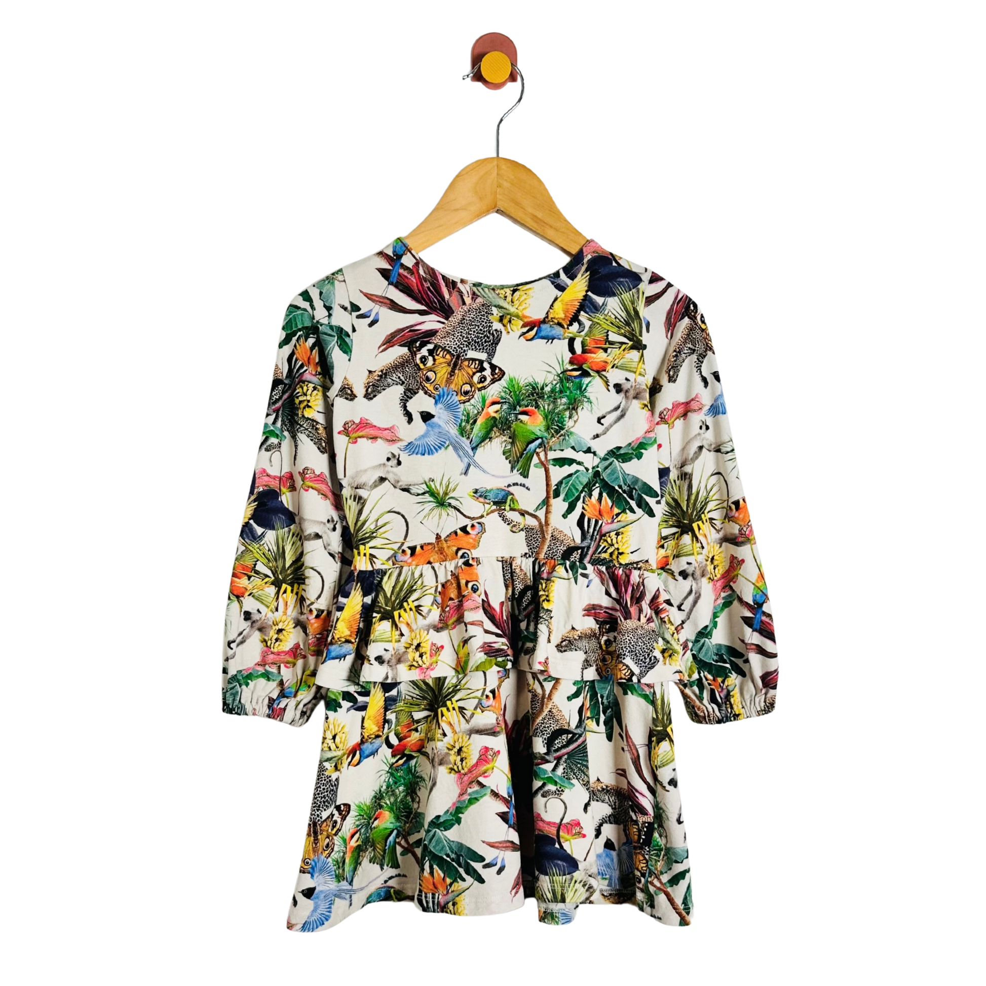 A long-sleeve children's dress with a vibrant multicolor dinosaur and jungle print on a cream background, hanging on a wooden hanger against a plain white background.