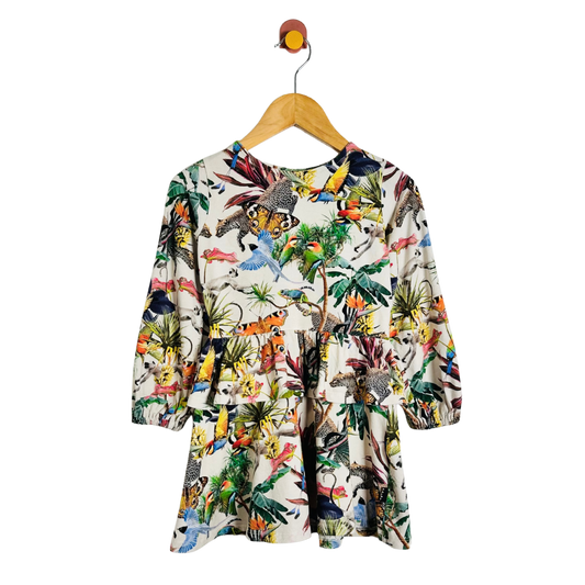 A long-sleeve children's dress with a vibrant multicolor dinosaur and jungle print on a cream background, hanging on a wooden hanger against a plain white background.