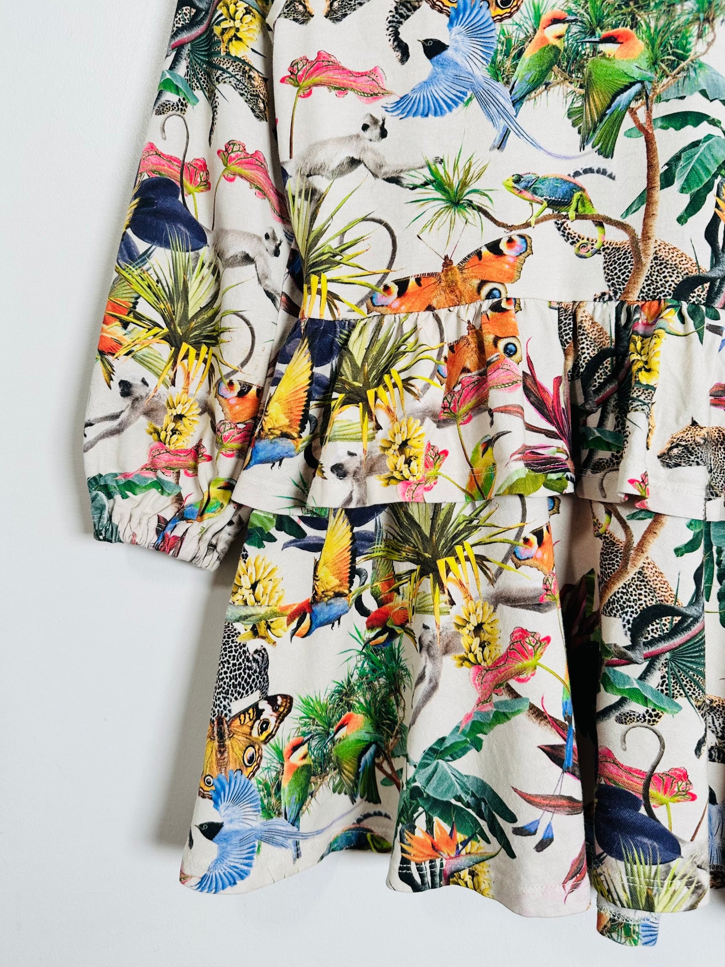 A tiered ruffle dress featuring a vibrant, multicolor jungle and animal print on a cream background, with long sleeves and a ruffled waist.