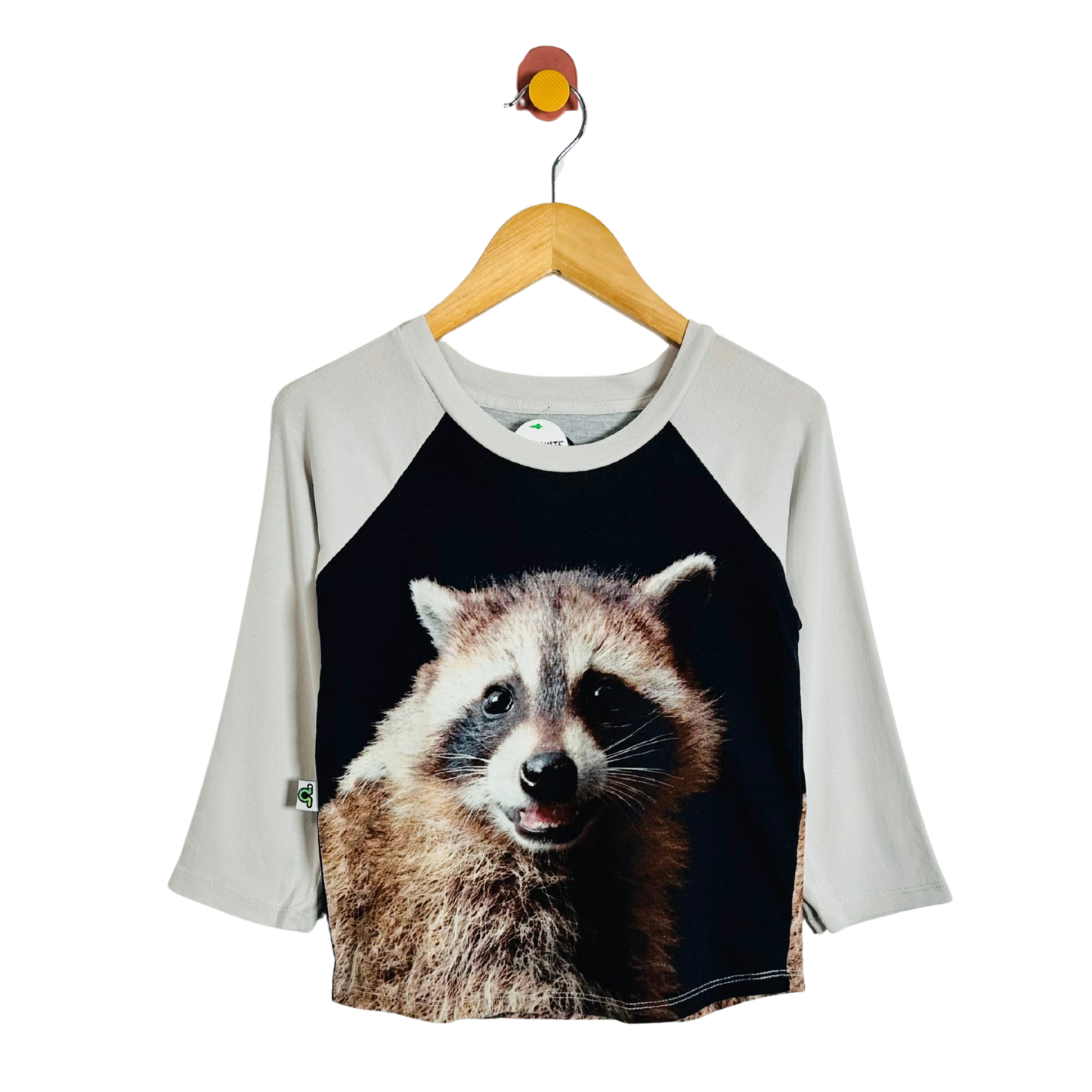 A raglan t-shirt for kids, featuring a large printed raccoon face on the front over a black body and light gray sleeves, hanging on a wooden hanger against a white background.