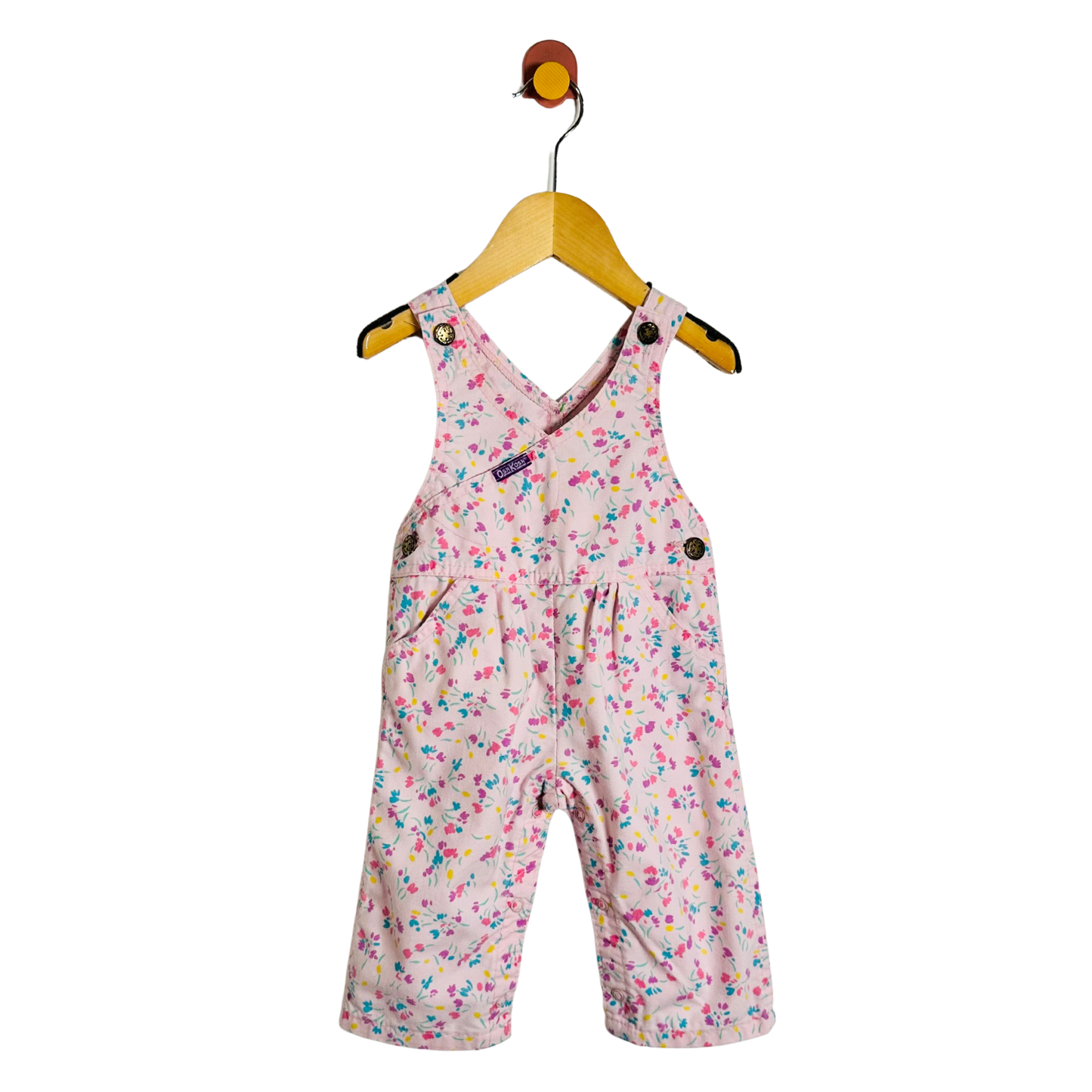 A baby girl's pink overall romper with a colorful floral print, hanging on a wooden hanger against a plain white background.