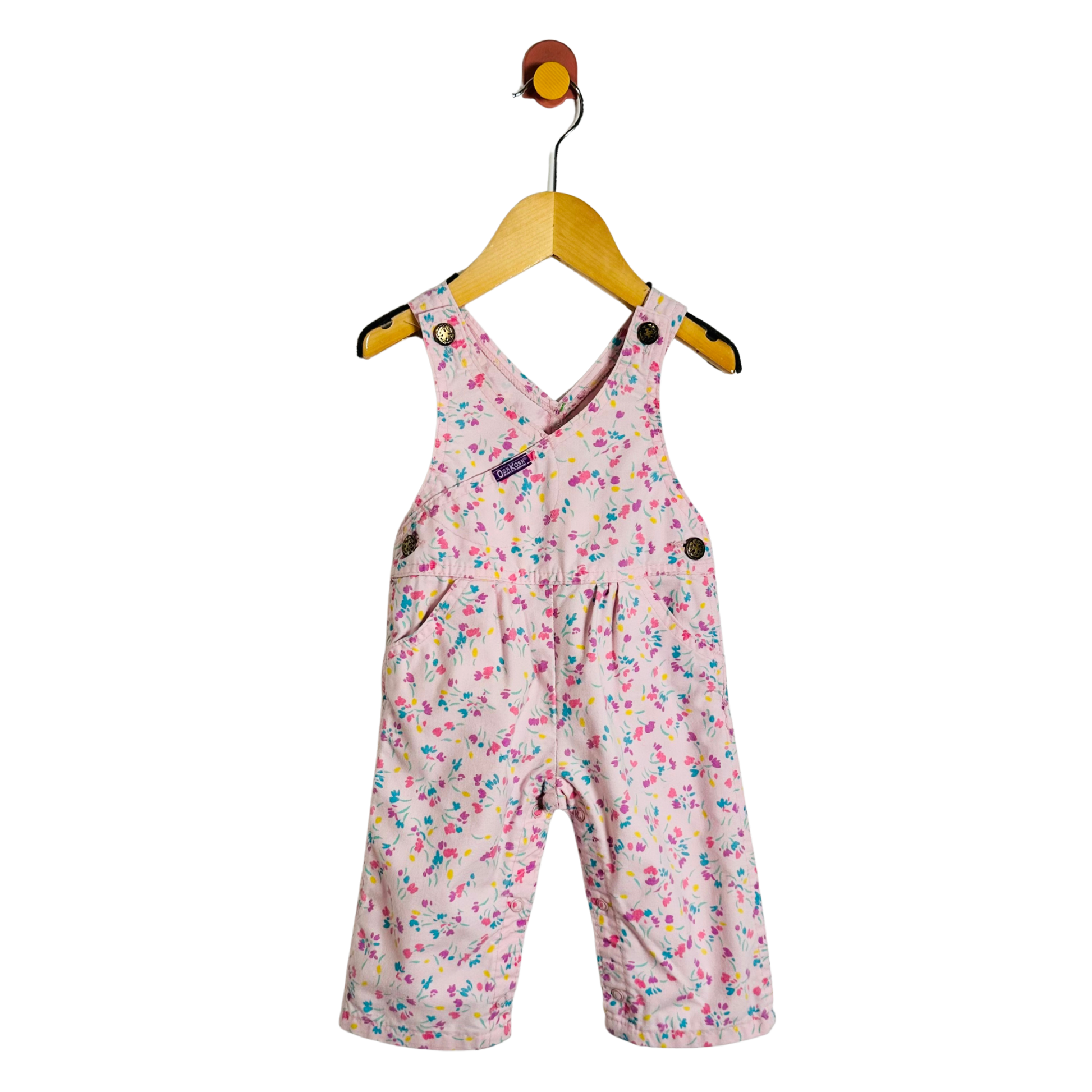 A baby girl's pink overall romper with a colorful floral print, hanging on a wooden hanger against a plain white background.