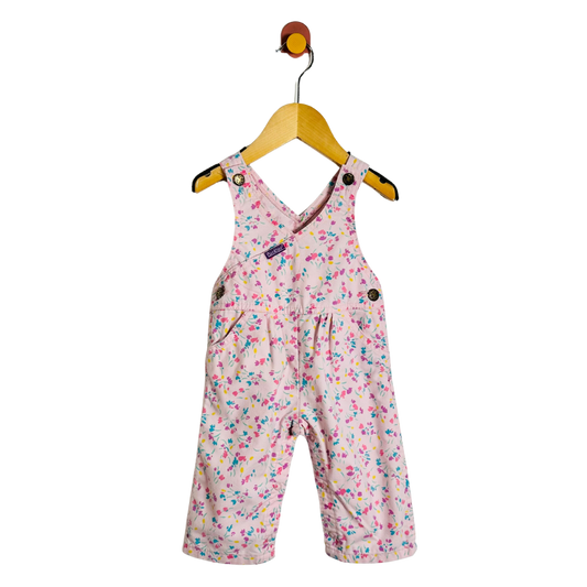 A baby girl's pink overall romper with a colorful floral print, hanging on a wooden hanger against a plain white background.