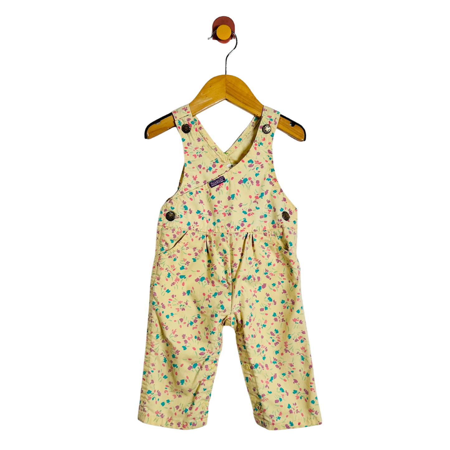 A baby romper in a yellow color with a colorful floral print, hanging on a wooden hanger against a plain white background.