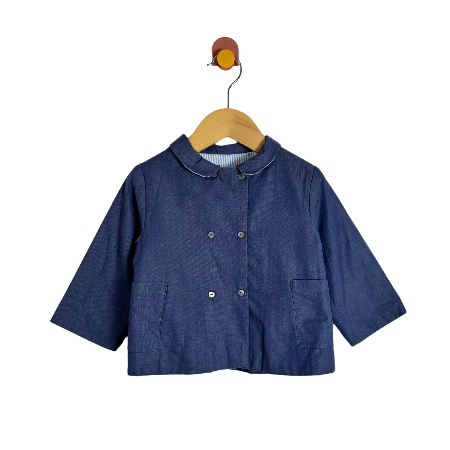 A dark blue denim-like children's jacket with a Peter Pan collar and double-breasted buttons, hanging on a wooden hanger against a plain white background.