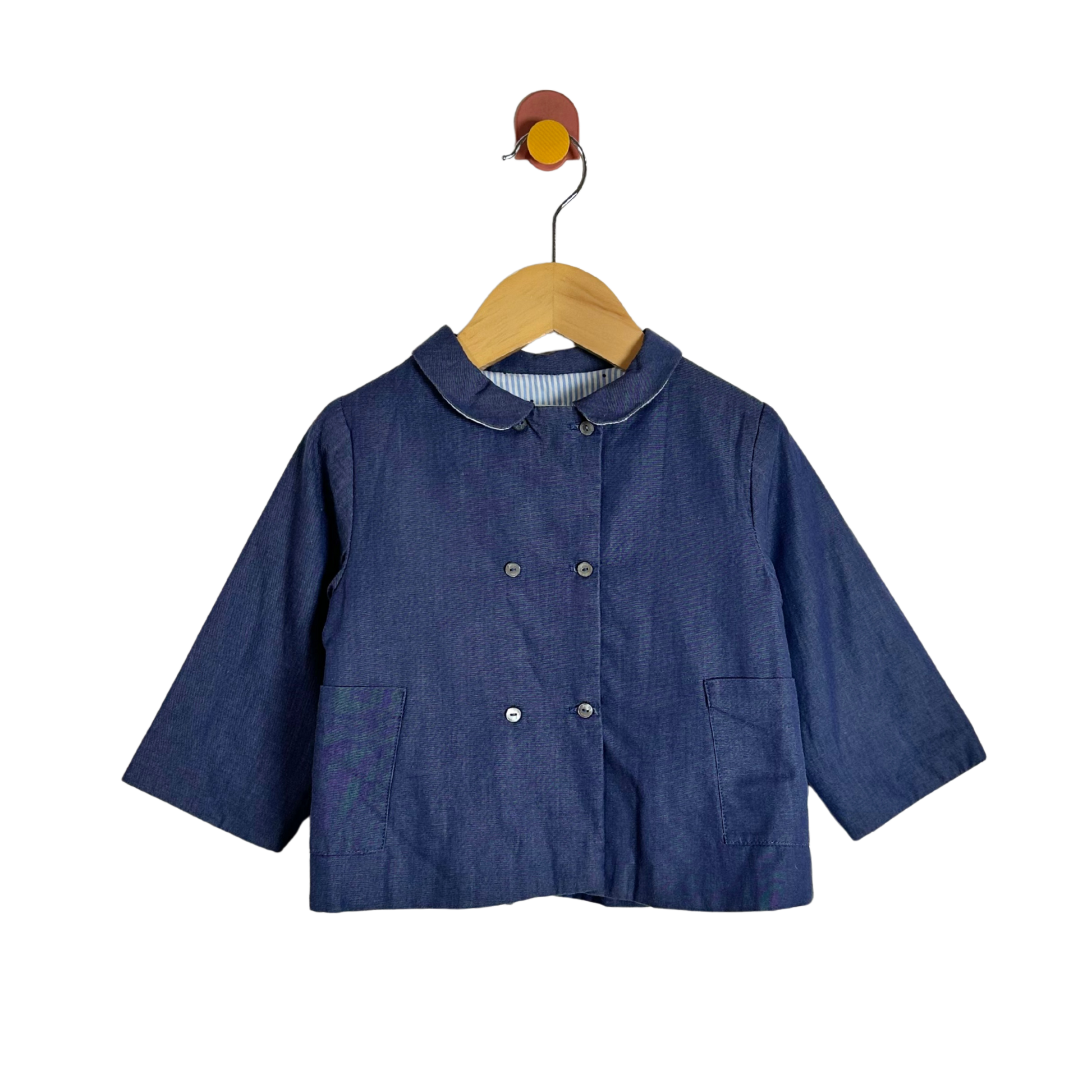 A dark blue denim-like children's jacket with a Peter Pan collar and double-breasted buttons, hanging on a wooden hanger against a plain white background.