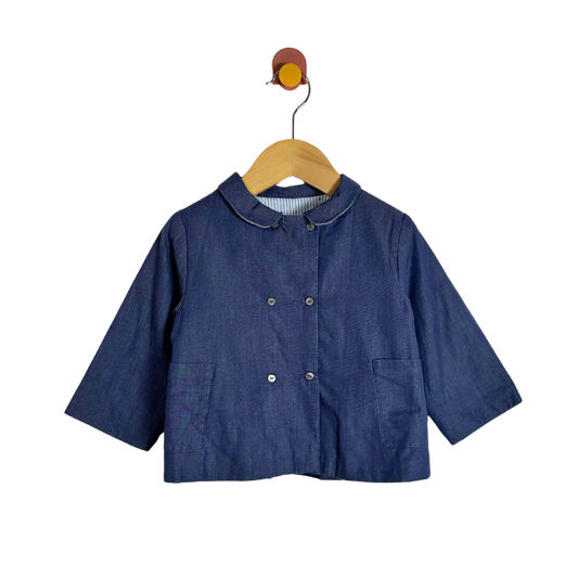 A dark blue denim-like children's jacket with a Peter Pan collar and double-breasted buttons, hanging on a wooden hanger against a plain white background.
