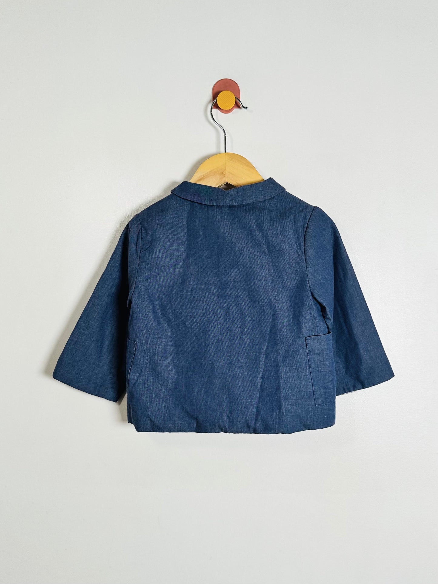 A navy blue textured fabric short-sleeve top or jacket displayed on a wooden hanger against a plain light gray wall.