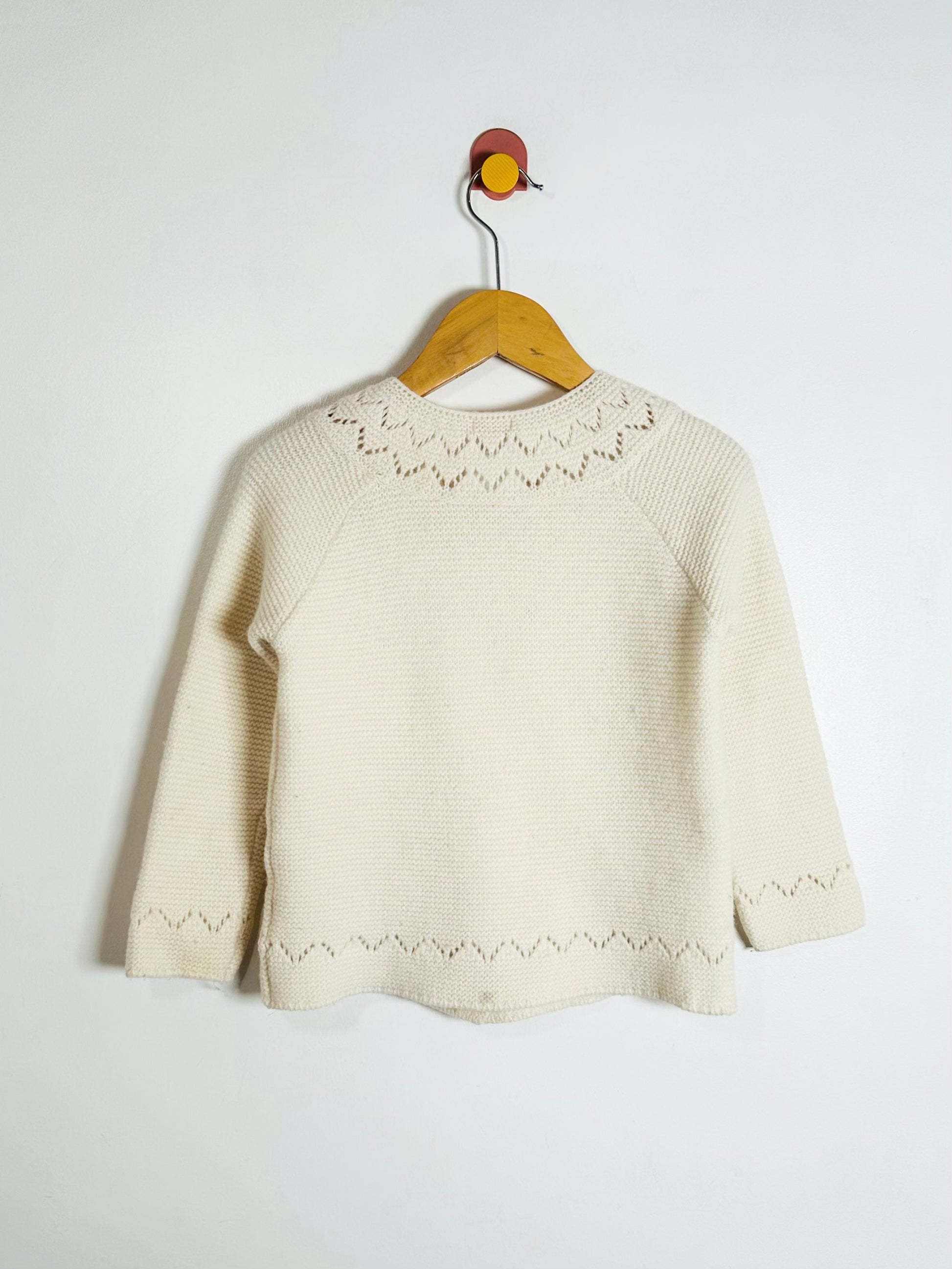 White knitted sweater on a wooden hanger against a white background