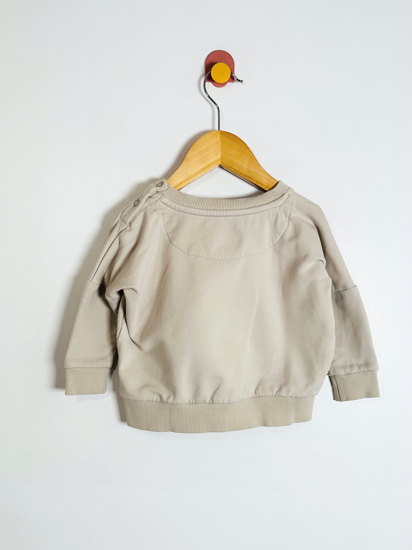 Beige sweatshirt on a wooden hanger against a white background