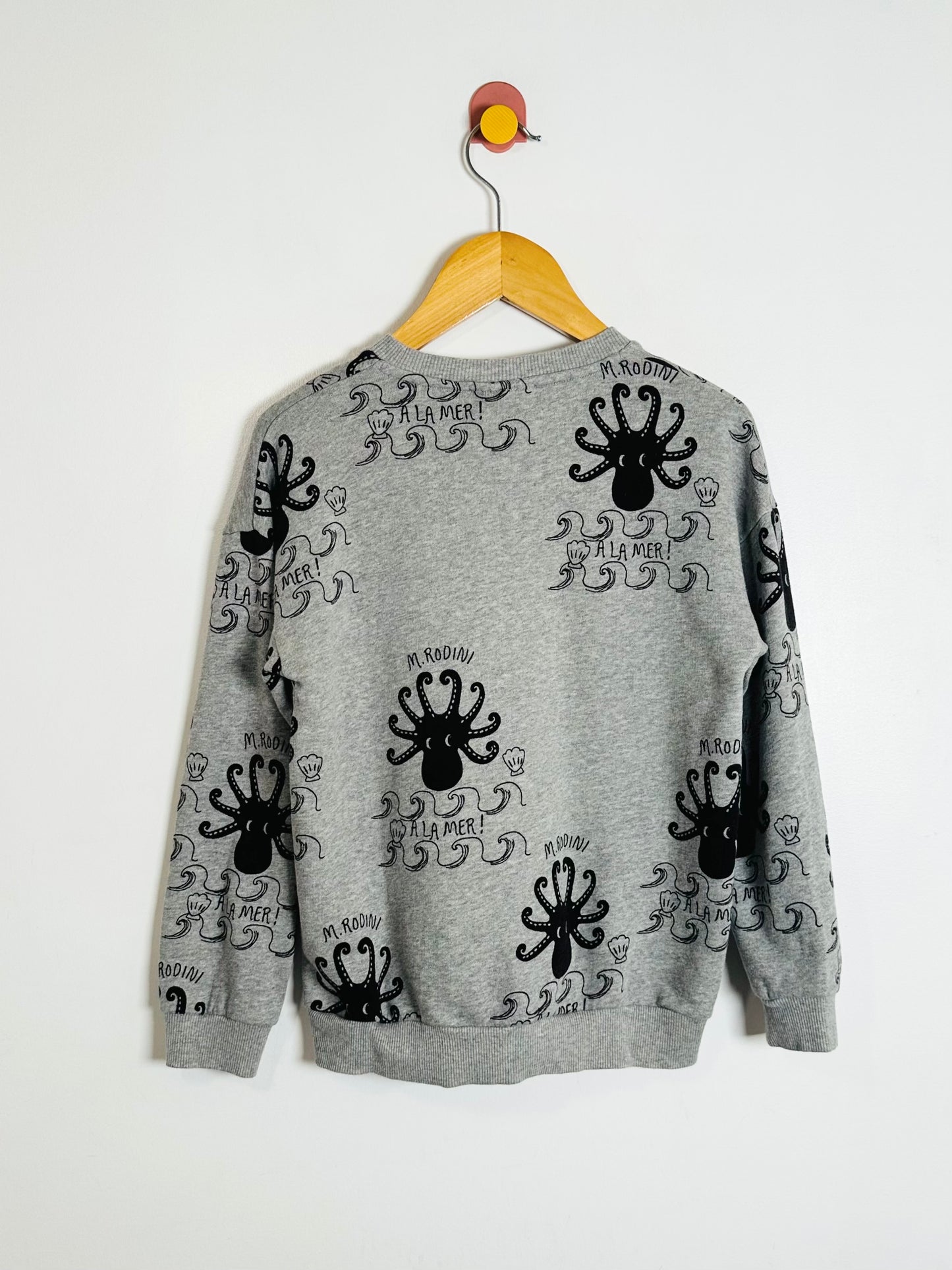 Gray sweater with black octopus designs on a hanger against a white background