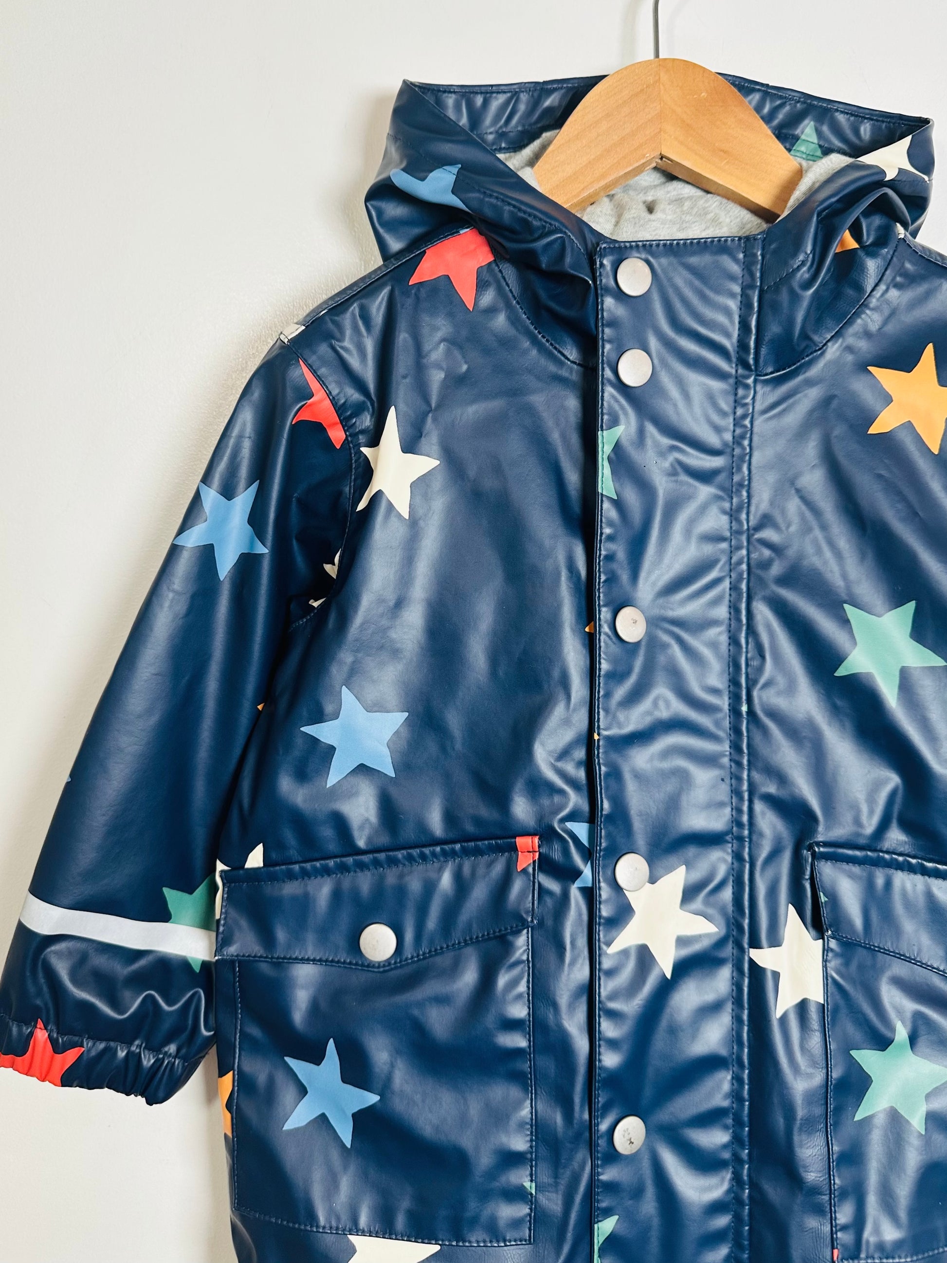 Navy blue raincoat with colorful star patterns on a wooden hanger against a white background