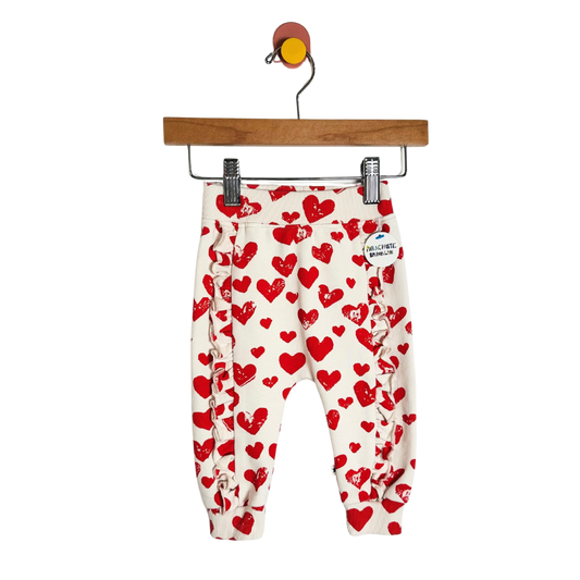 White pants with red heart patterns hanging on a wooden hanger against a white background