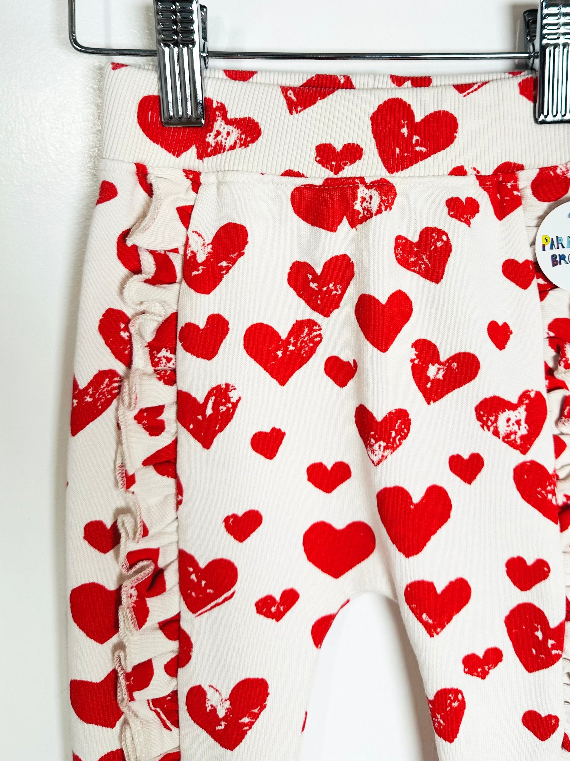 White pants with red heart patterns hanging on a rack.