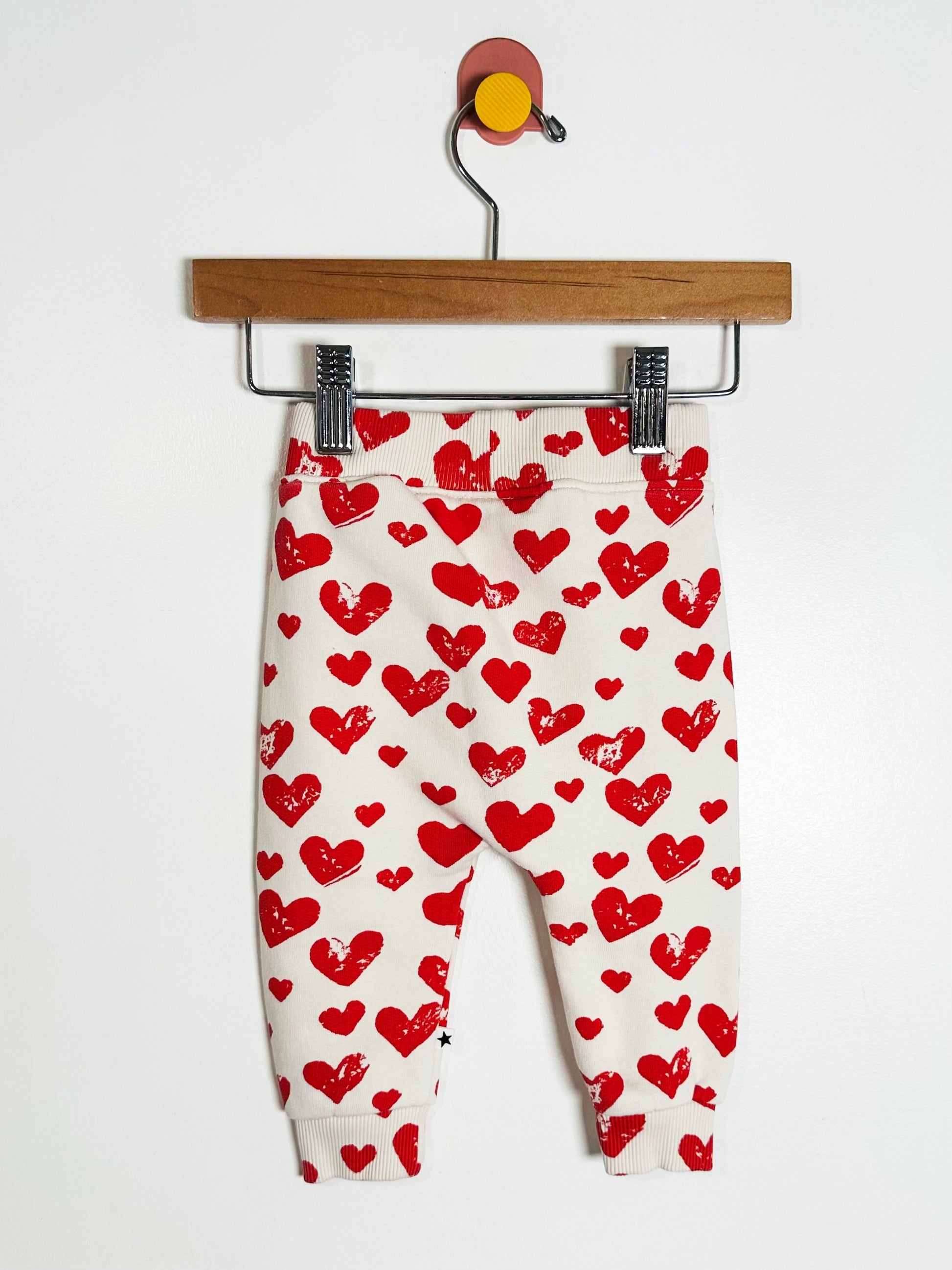 White pants with red heart pattern on a hanger against a white background