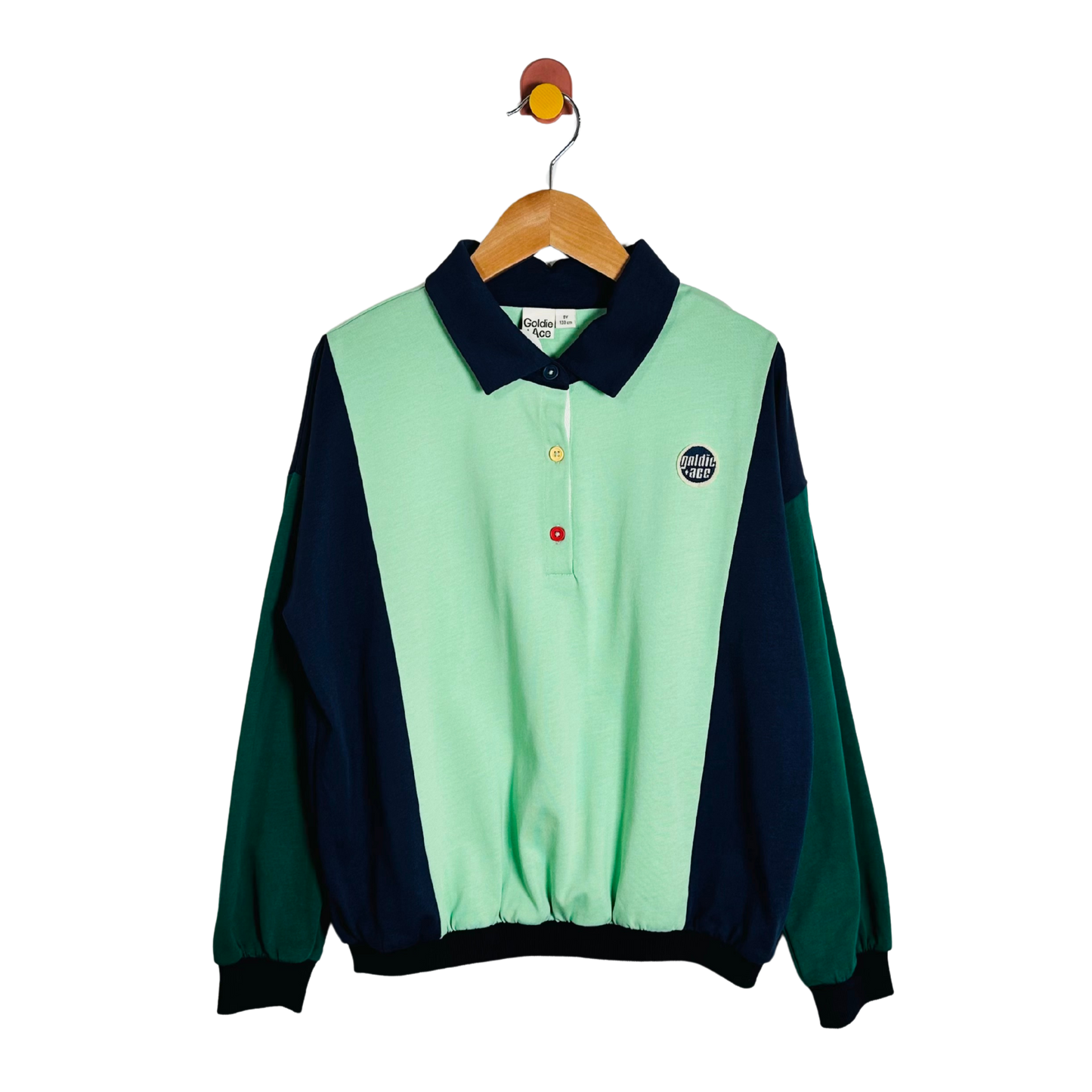 A colorblock long-sleeve polo shirt hanging on a wooden hanger against a white background. The shirt features a mint green body, dark navy blue collar and side panels, and forest green sleeves.