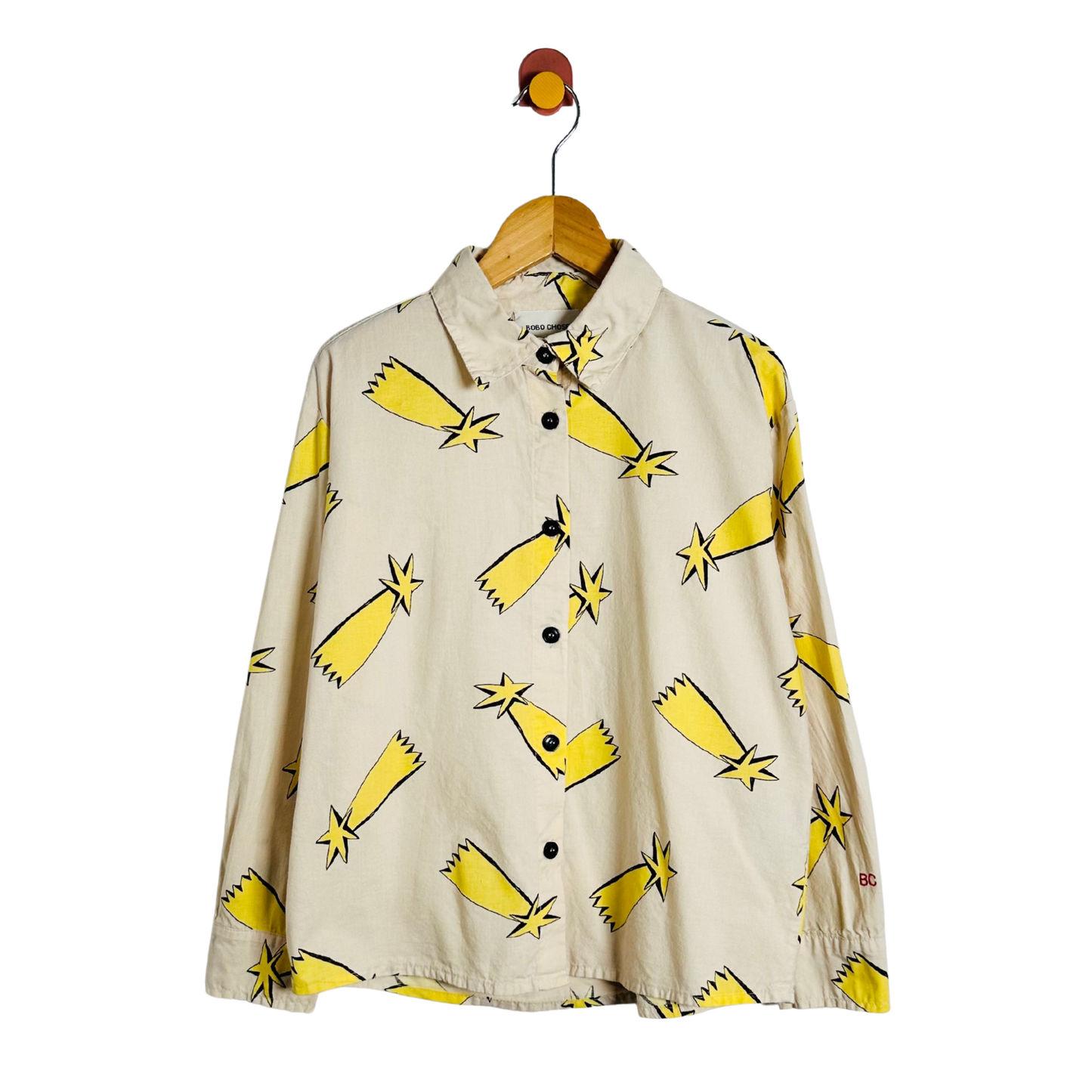 A beige long-sleeve button-up shirt with a yellow and black starburst pattern, hanging on a wooden hanger against a white background.