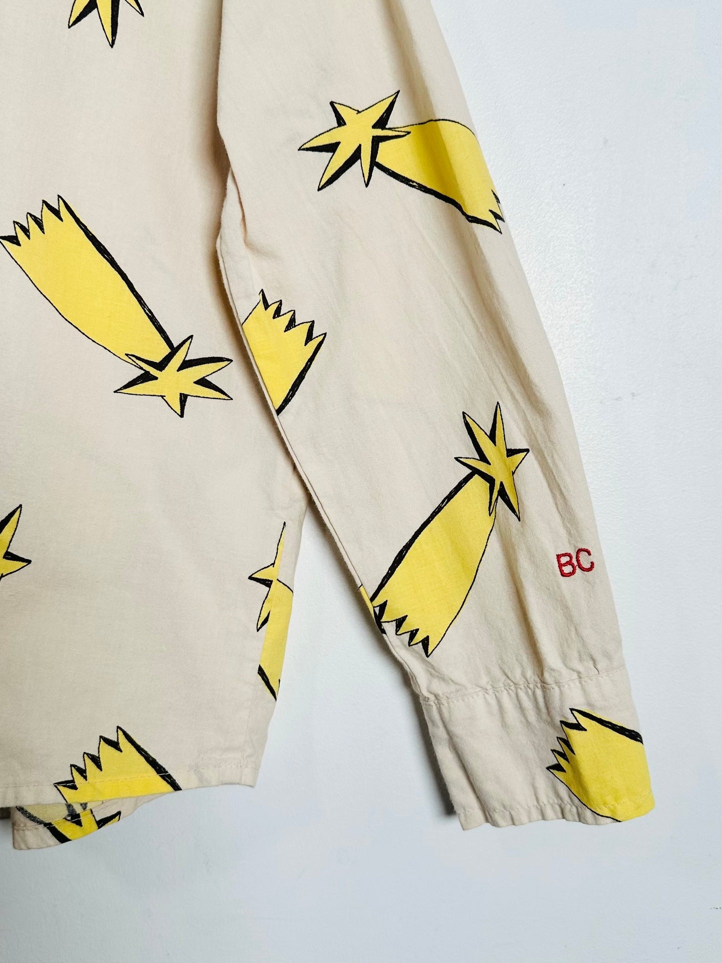 Beige long-sleeve jacket with a yellow and black shooting star print, featuring a small red 'BC' logo on the cuff.