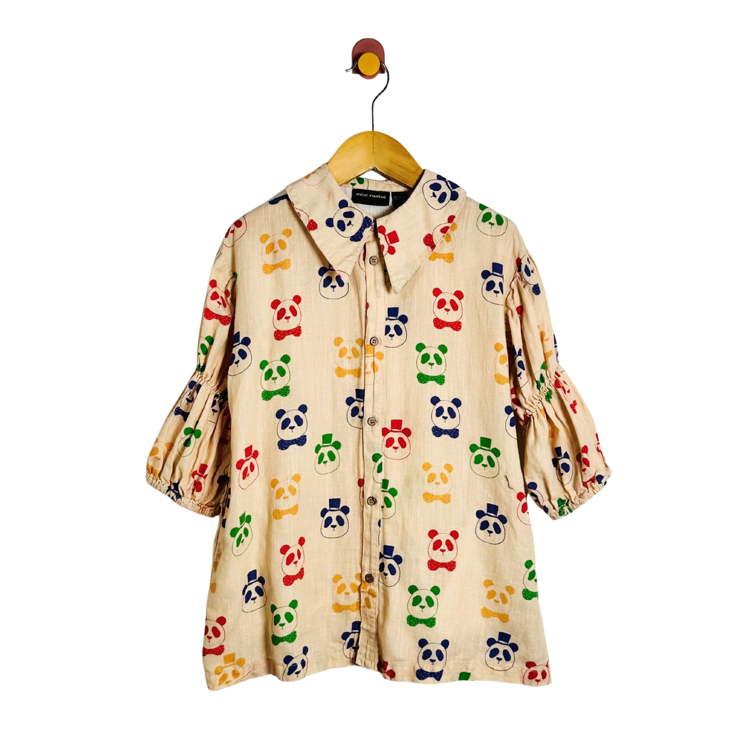 A cream-colored cotton dress with an all-over colorful panda print, hanging on a wooden hanger with a metal hook.