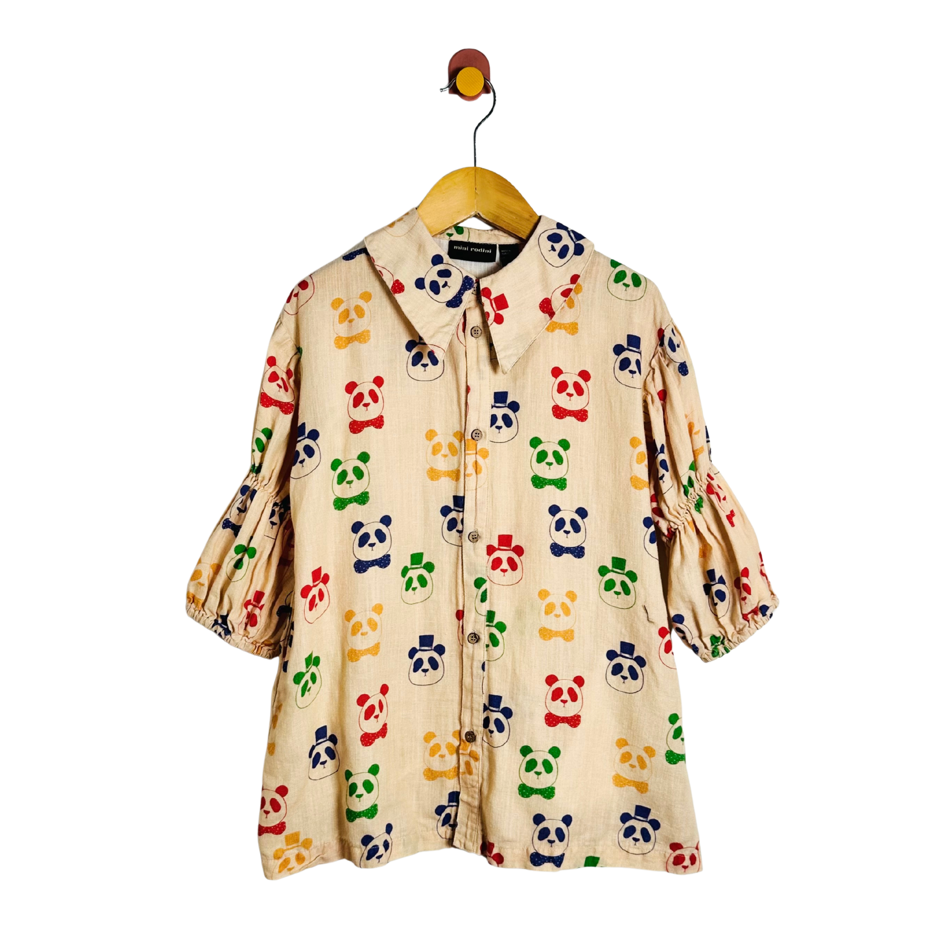 A cream-colored cotton dress with an all-over colorful panda print, hanging on a wooden hanger with a metal hook.