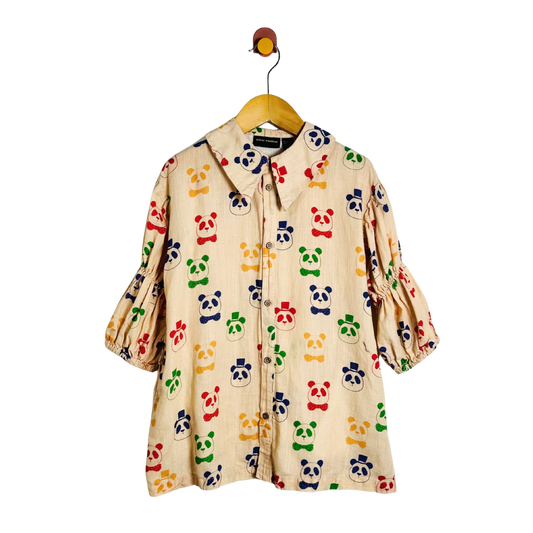 A cream-colored cotton dress with an all-over colorful panda print, hanging on a wooden hanger with a metal hook.