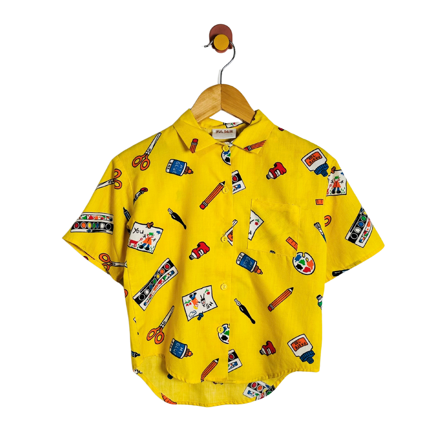 A yellow short-sleeve button-up shirt with an all-over colorful craft-themed print, hanging on a wooden hanger with a brown hook against a plain white background.
