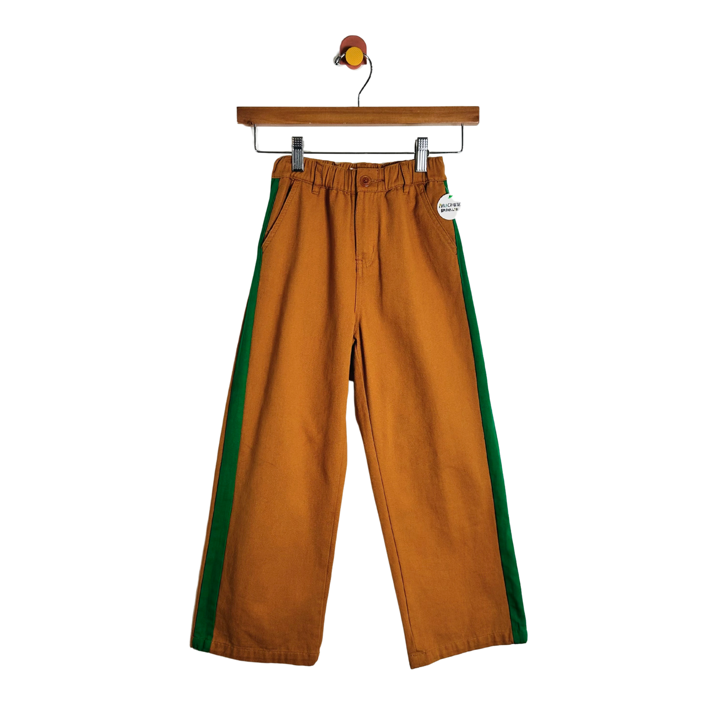 A pair of wide-leg brown pants with green side stripes, hanging from a wooden hanger against a plain white background.