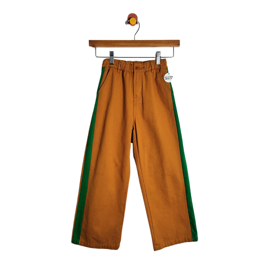 A pair of wide-leg brown pants with green side stripes, hanging from a wooden hanger against a plain white background.