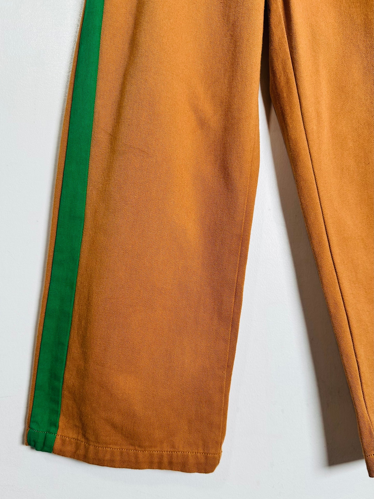 Close-up of a pair of wide-leg brown pants with a vibrant green side stripe, laid flat against a light gray background.