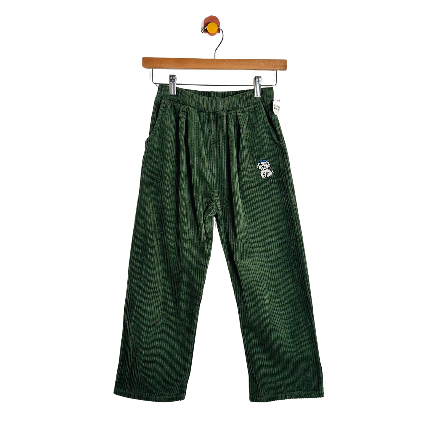 Dark green corduroy pants with an elastic waistband and a small embroidered dog patch on the left hip, hanging from a wooden hanger against a white background.