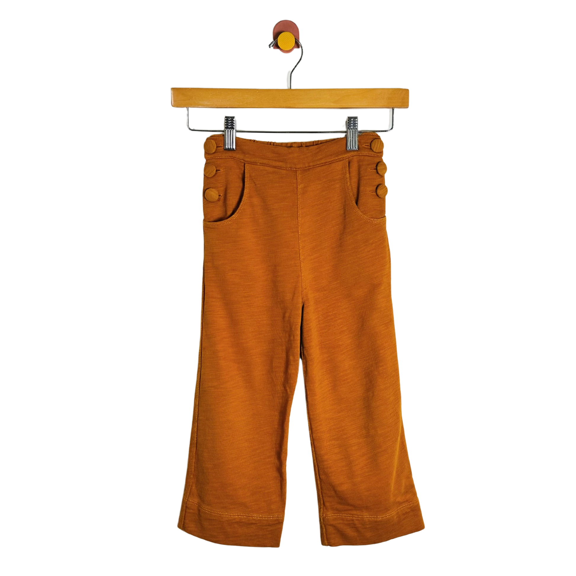 A pair of wide-leg cropped pants in a warm rust-orange corduroy fabric, hanging from a wooden hanger against a plain white background.