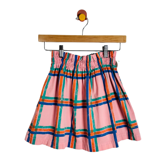 A pink pleated skirt with a colorful plaid pattern in blue, orange, and green, hanging from a wooden hanger against a white background.