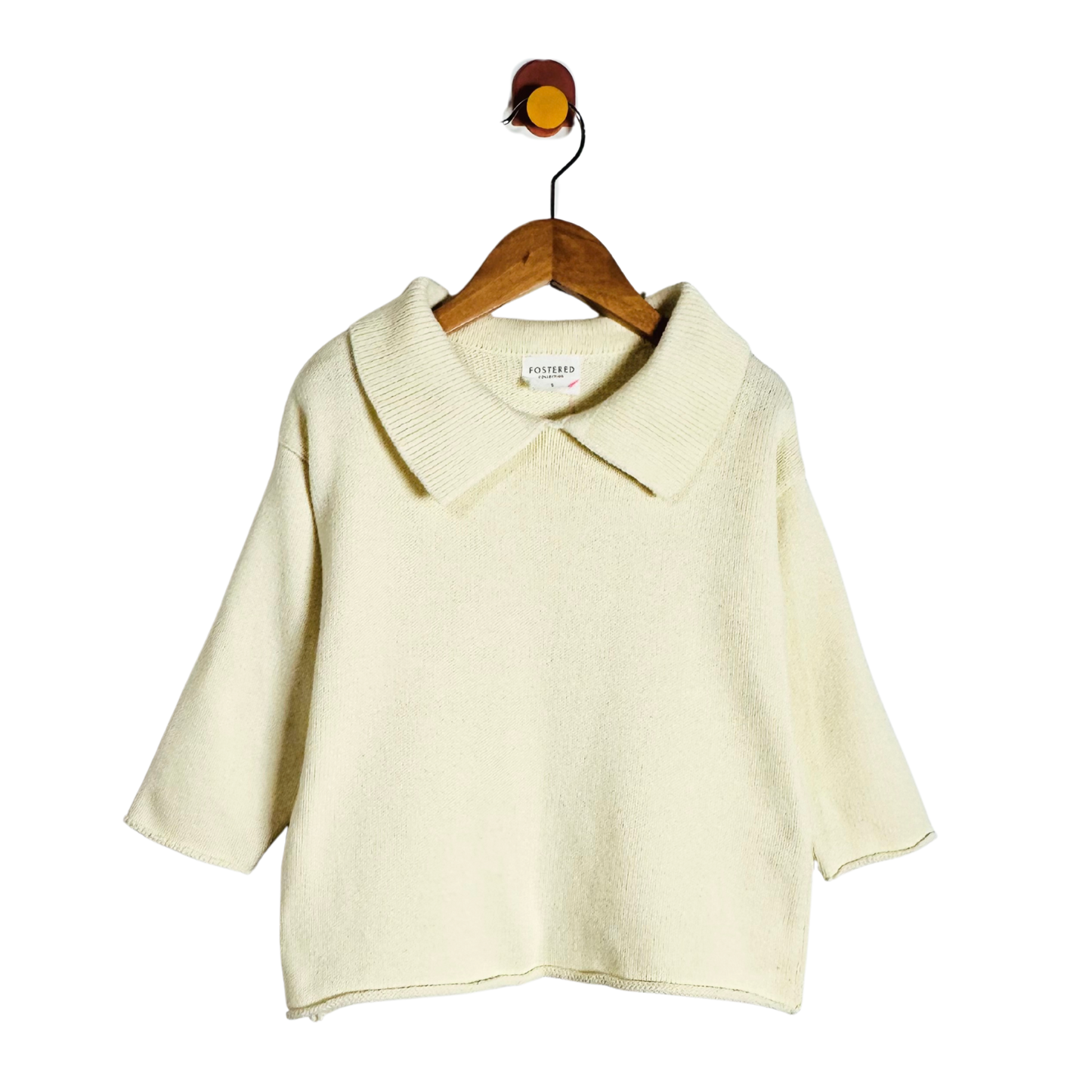 A cream-colored knit short-sleeve top with a wide collar, hanging on a wooden hanger against a plain white background.