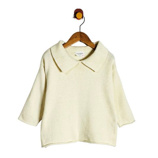 A cream-colored knit short-sleeve top with a wide collar, hanging on a wooden hanger against a plain white background.
