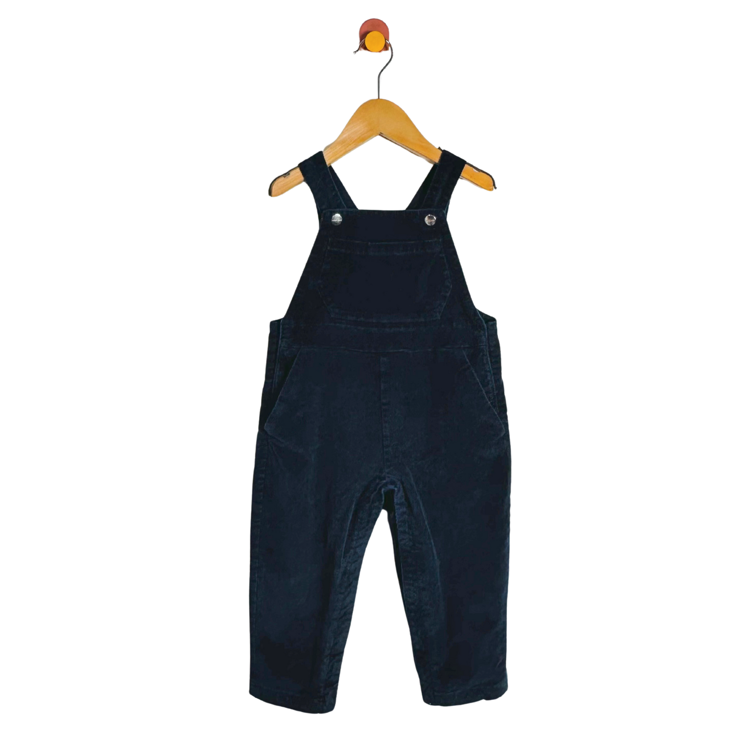 A pair of dark navy blue corduroy baby overalls hanging on a wooden hanger against a plain white background.
