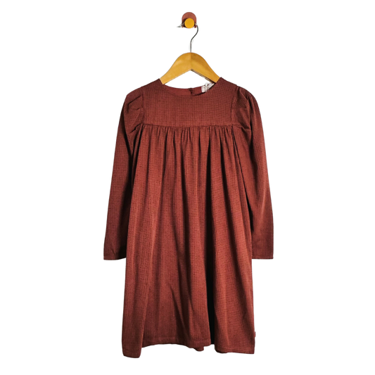 A rust-colored long-sleeve dress with a textured pattern, hanging on a wooden hanger against a plain white background.