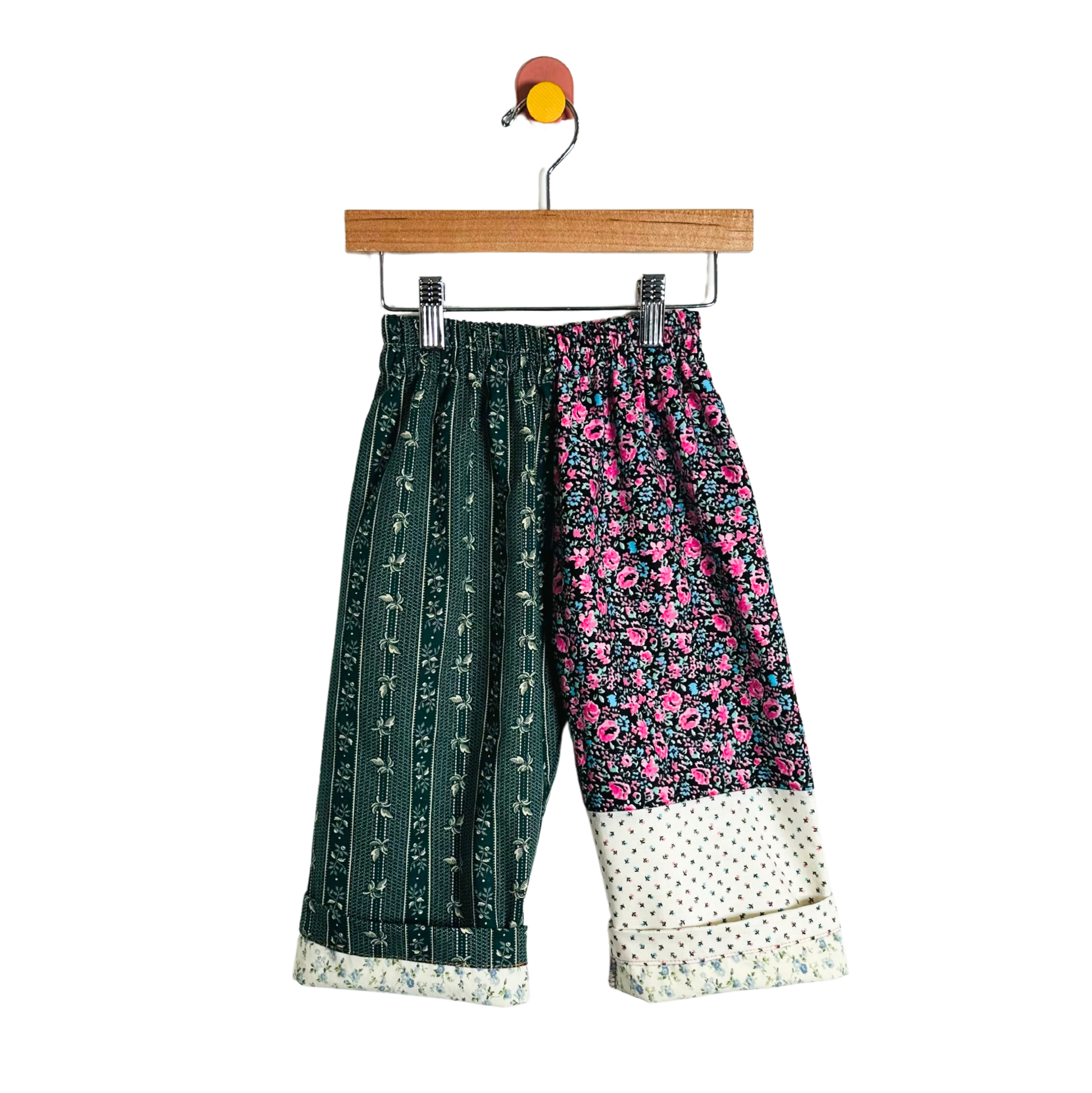 Colorful patchwork pants on a hanger against a white background