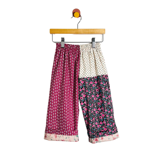 Color-blocked pants with floral and polka dot patterns on a hanger against a white background