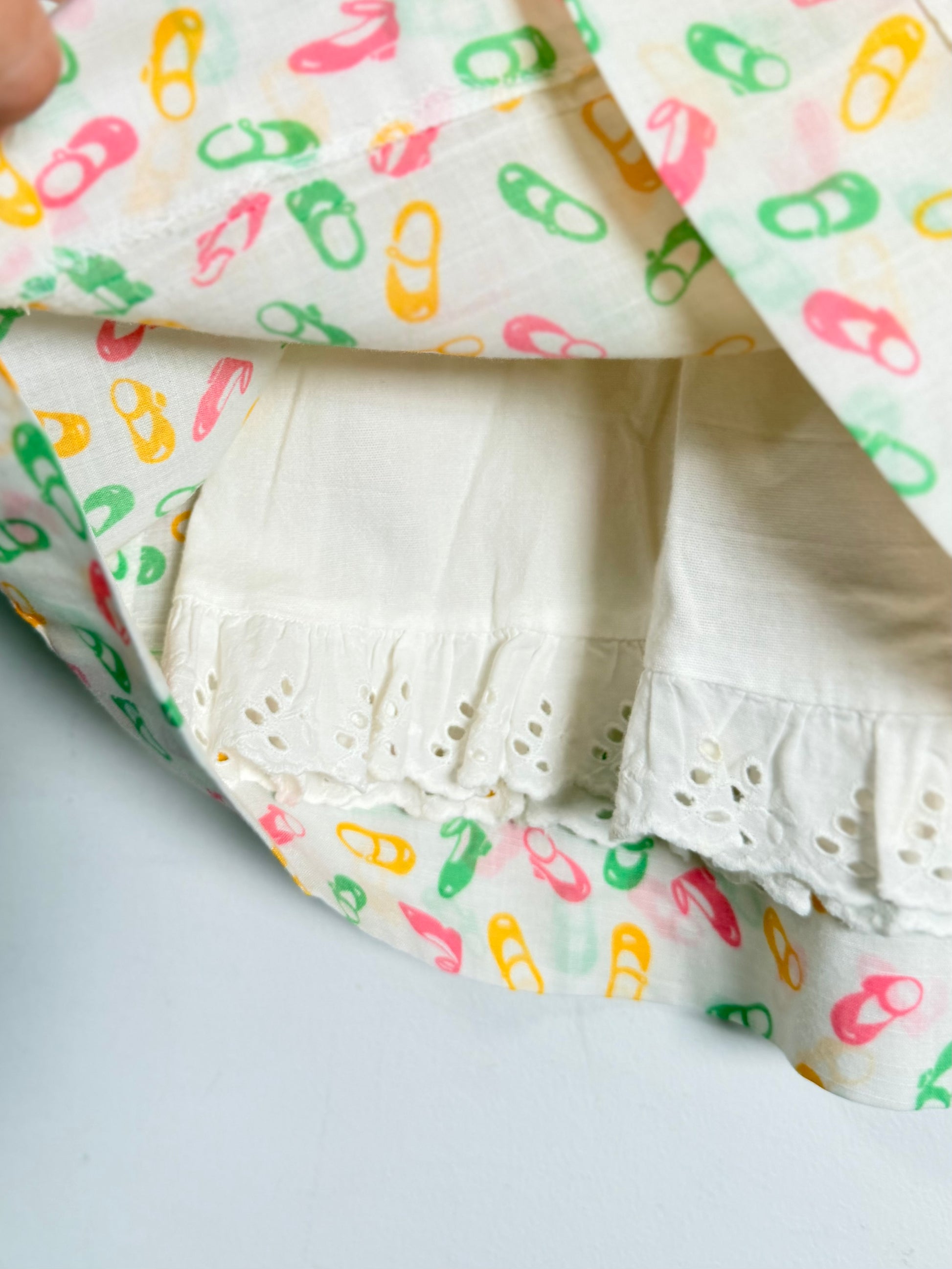 A close-up of a white fabric garment with a colorful pattern in pink, green, and yellow, featuring eyelet lace trim.