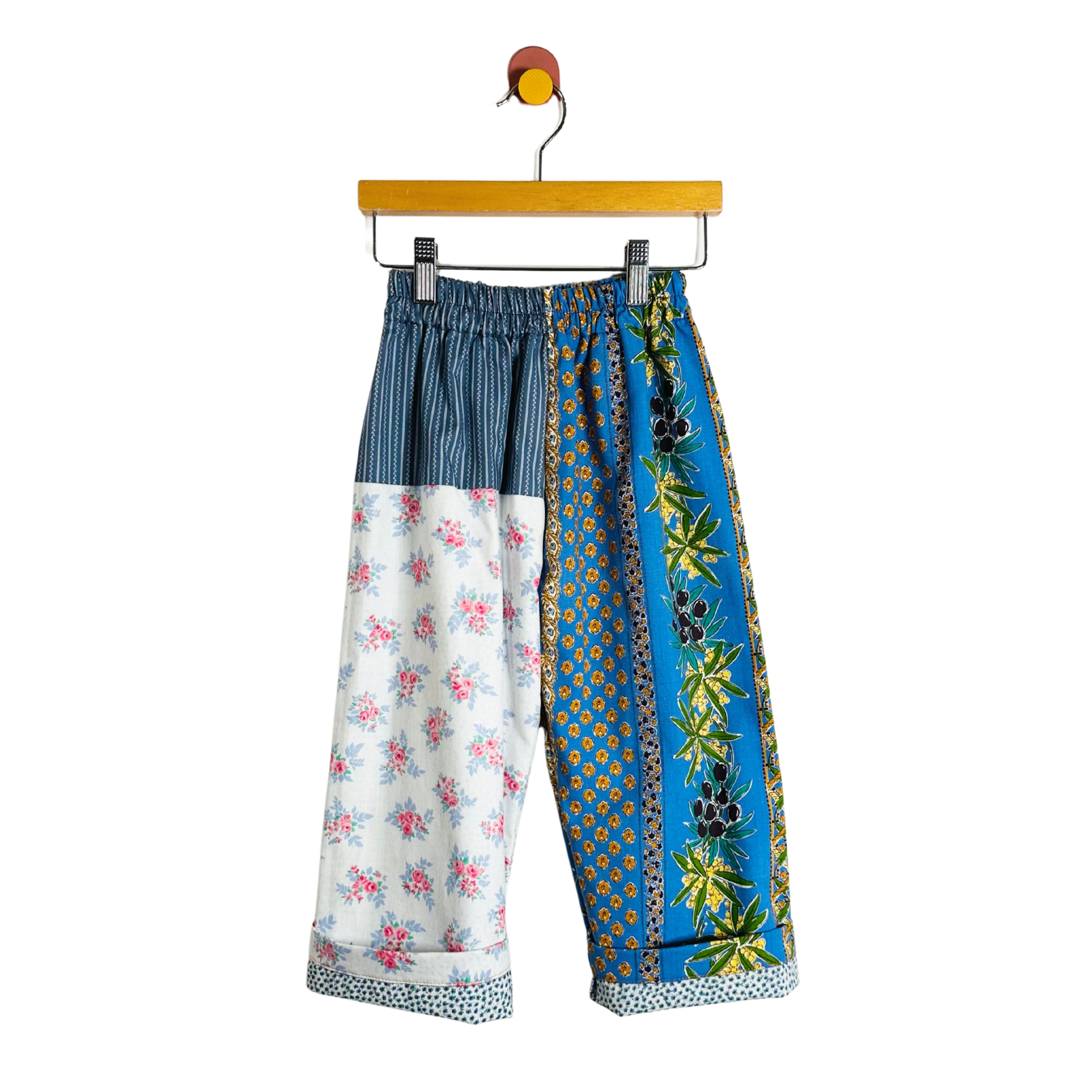 Colorful patchwork pants on a hanger against a white background